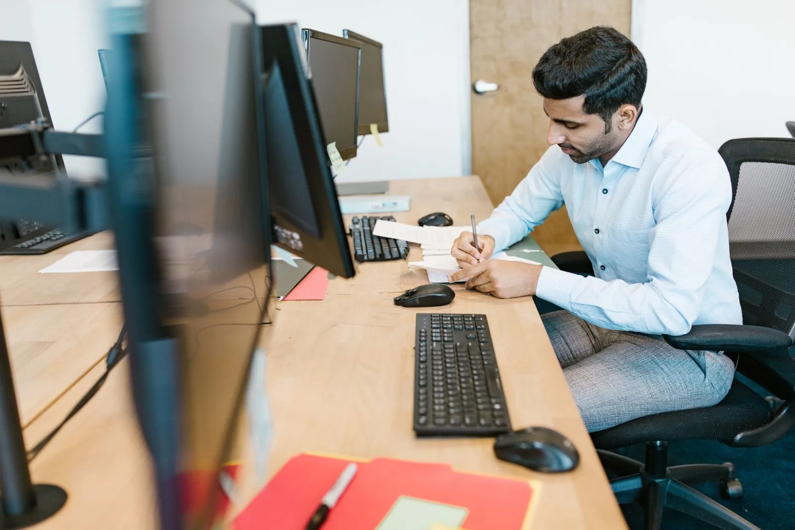 A staff member making notes beside a computer at an office desk.