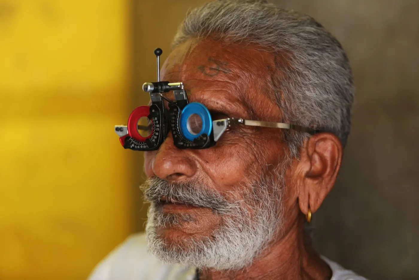 A senior Indian man wearing an optometrist's trial frame during an eye test.