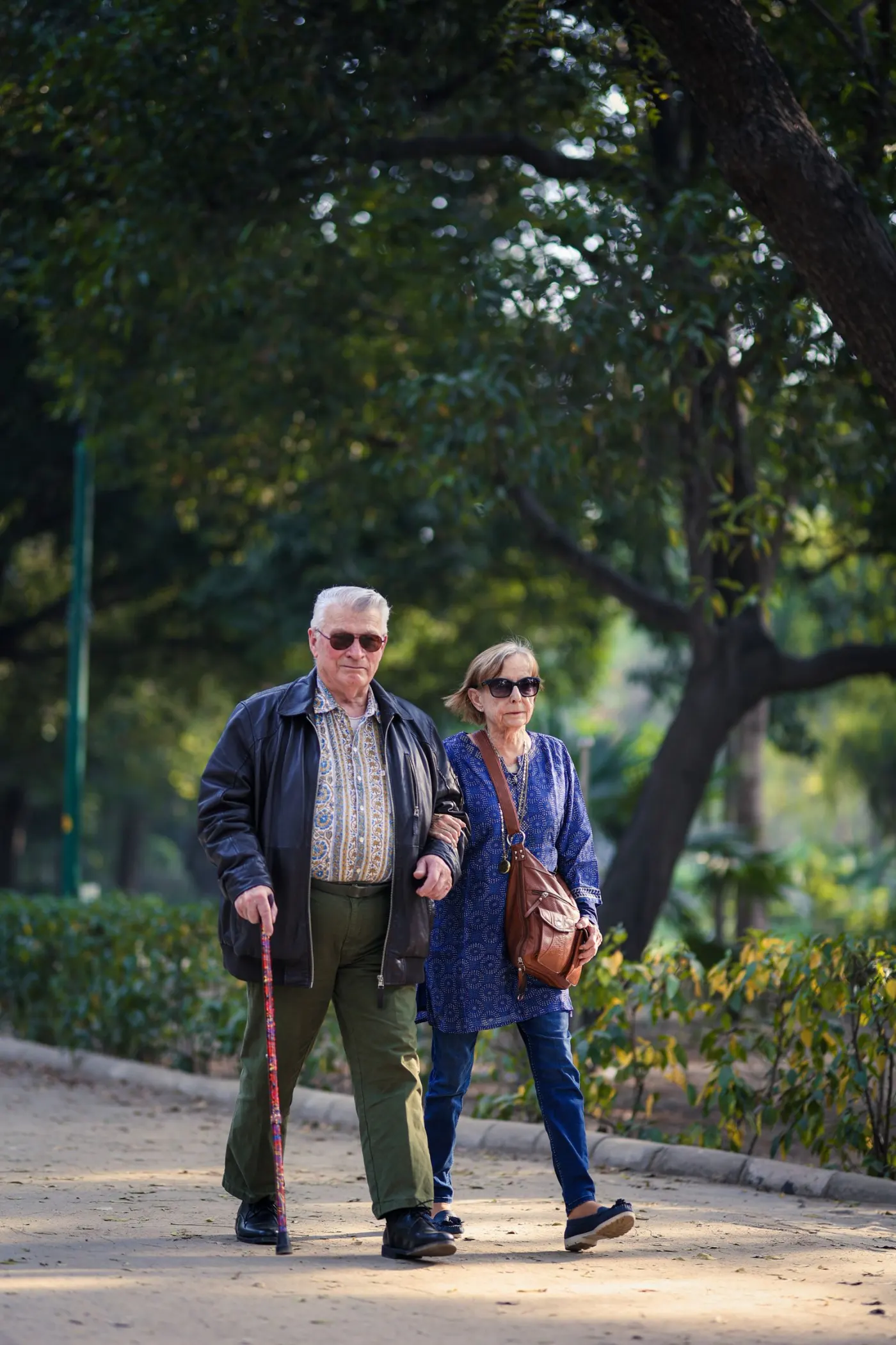 An elderly couple walking together with a cane in a park in New Delhi.